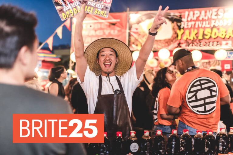 A food stall owner smiles and raises his hands in celebration
